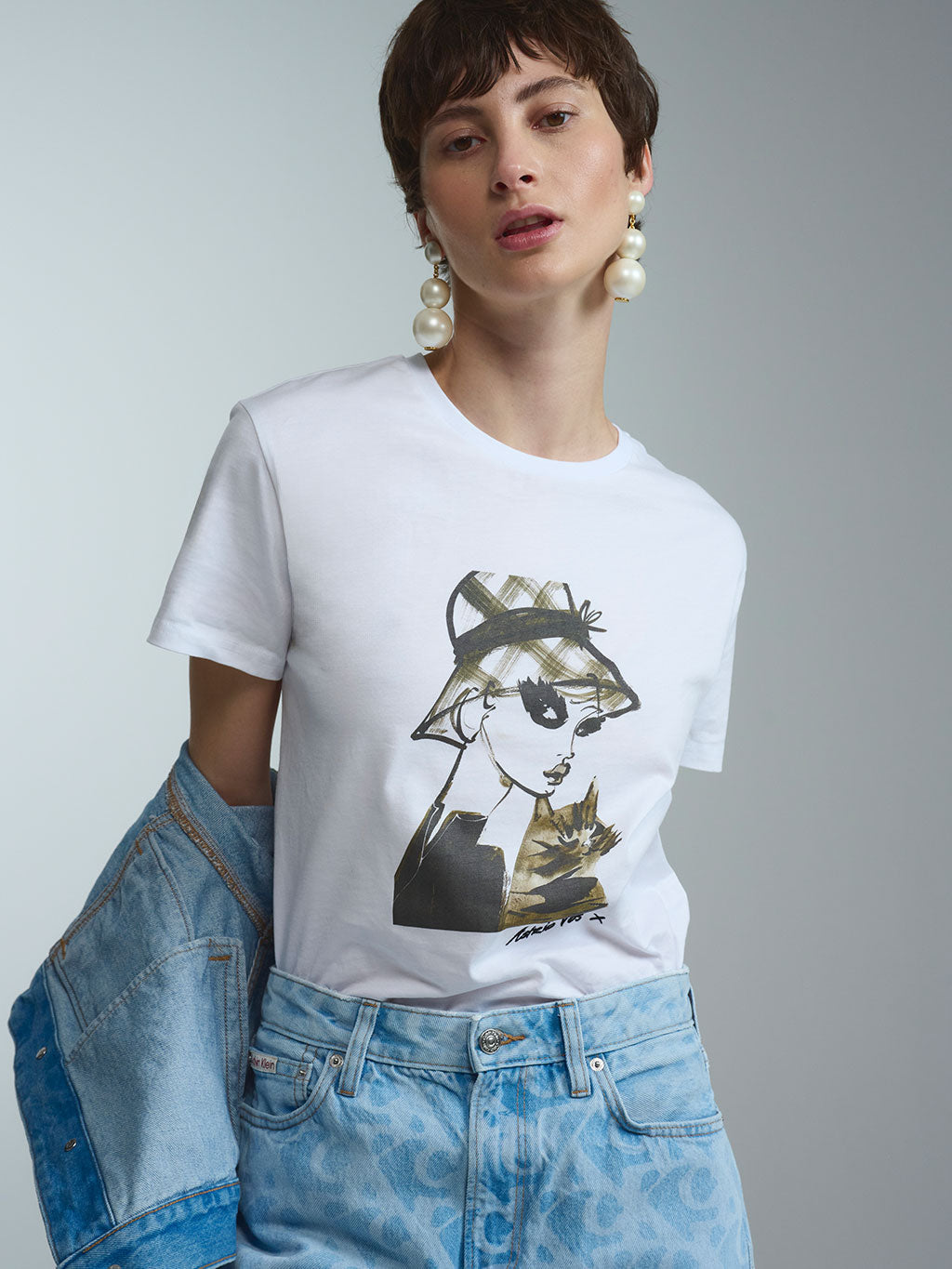 Exklusives weißes Damen-T-Shirt aus der limitierten RAILIN x Astrid Vos X Art Edition. Der hochwertige, aufwändige Art Print zeigt die ausdrucksstarke Modeillustration Innocent glance mit einer Frau im Karo-Hut und einer Katze als tragbares Kunstwerk.