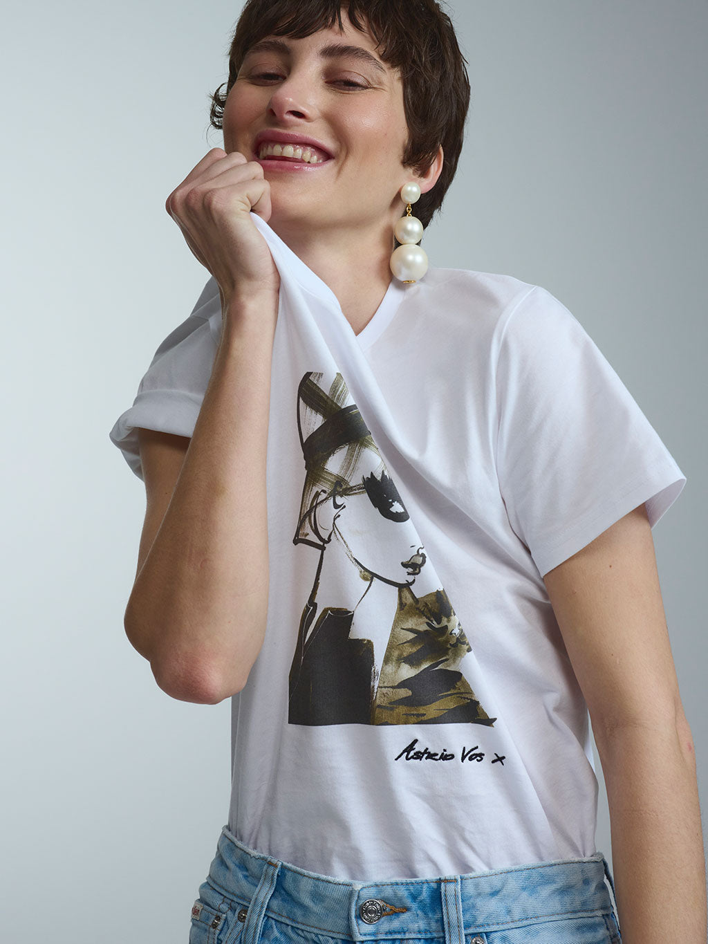 Modernes Statement-Piece aus den exklusiven RAILIN Künstler Edits: Limitiertes, hochwertig verarbeitetes Damen-T-Shirt in Weiß mit einem besonderen Art Print der Künstlerin Astrid Vos X, kombiniert mit einer gemusterten Jeans und großen Perlenohrringen.